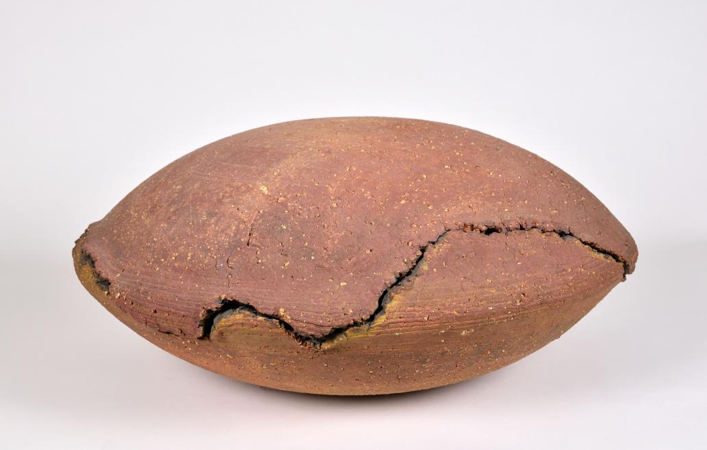 Oval-shaped clay vessel with cracks and a rough surface on a neutral background.