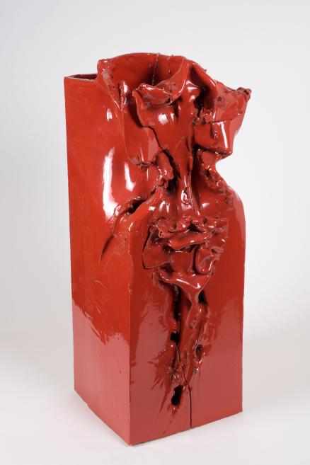 Bright red glossy ceramic object with a distorted, melted surface and cracks.