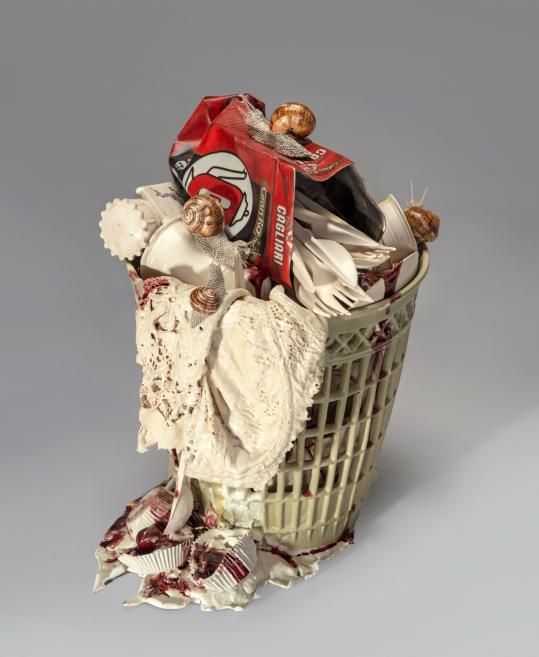 Ceramic sculpture shaped like a basket filled with plastic waste, snails, and organic textures.