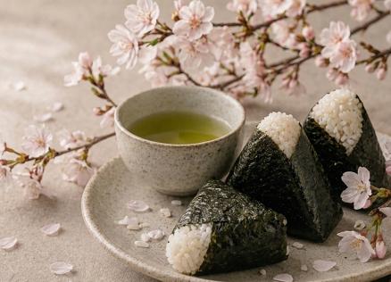 Plate with rice triangles (onigiri) and a cup of green tea, decorated with cherry blossom branches.