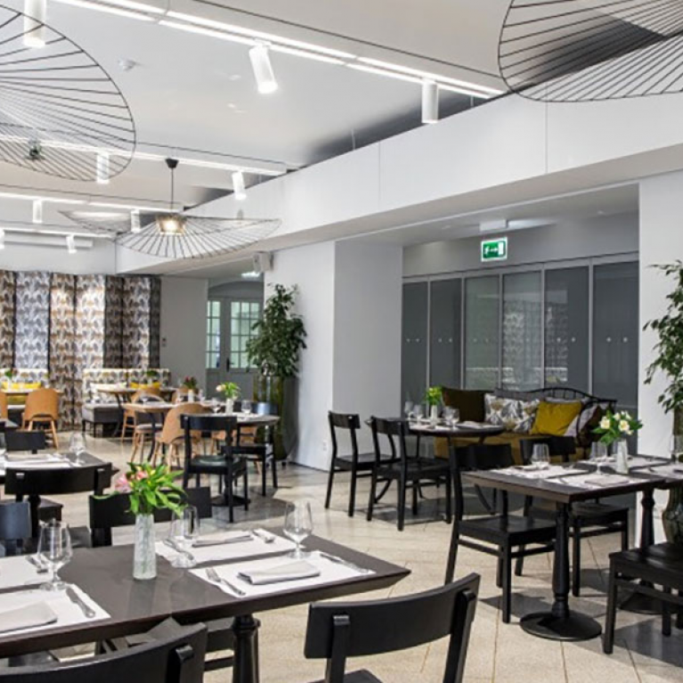 A bright and modern restaurant interior with set tables, black furniture, and decorative ceiling light fixtures.