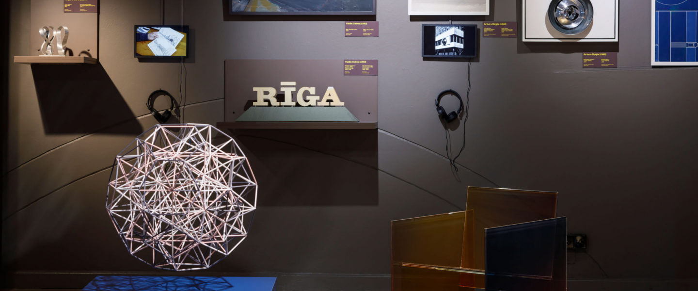 Izstādes ekspozīcijā redzams dizaina objektu, fotogrāfiju un multimediju darbu kopums ar izgaismotu telpisku struktūru priekšplānā un uzrakstu “RĪGA” centrā.
