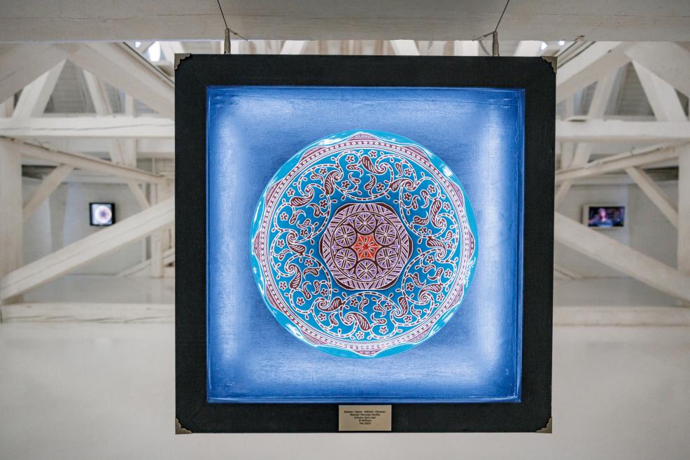 Bright blue and red patterned circular artwork displayed in a square illuminated frame.