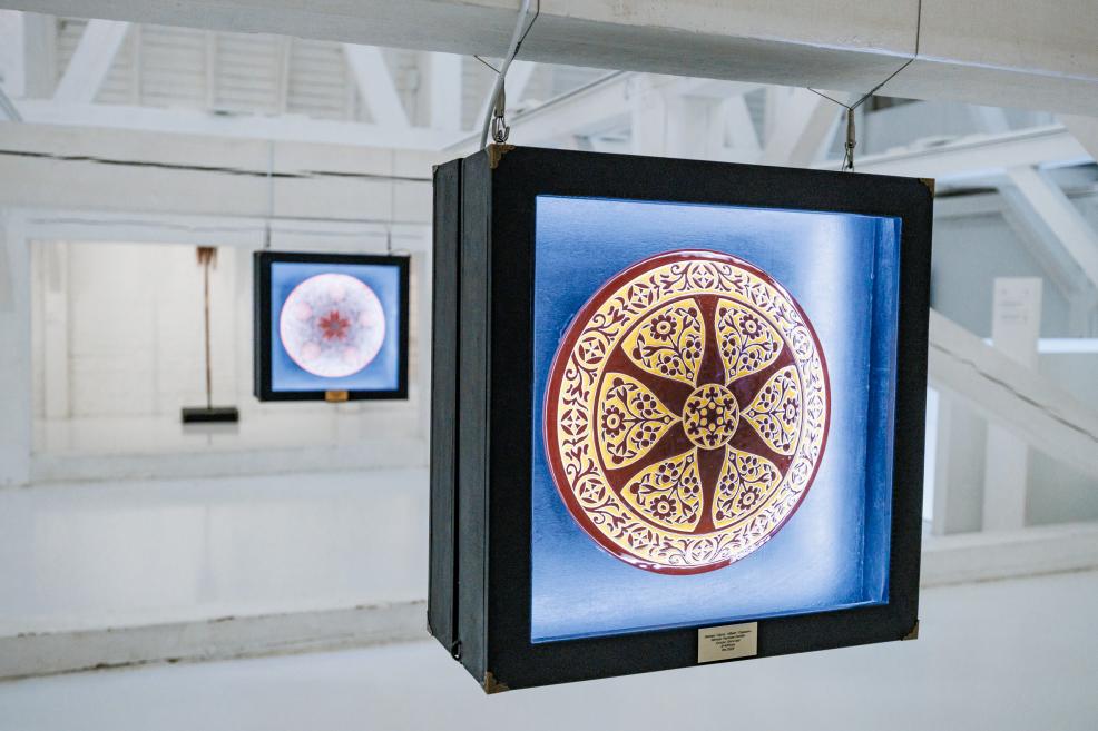 Izstādes “Qalqan. Krimas tatāru simboli” skats ar diviem izgaismotiem ornamentāliem šķīvjiem baltā telpā.