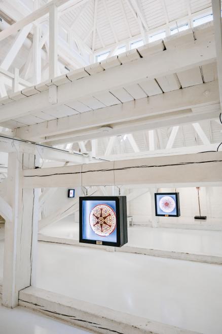 White wooden gallery interior with hanging illuminated circular artworks in perspective view.