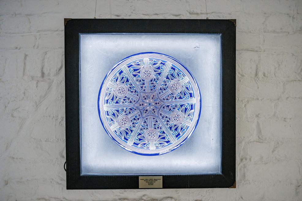 Close-up of an illuminated ceramic plate with red and blue floral ornament in a black frame.