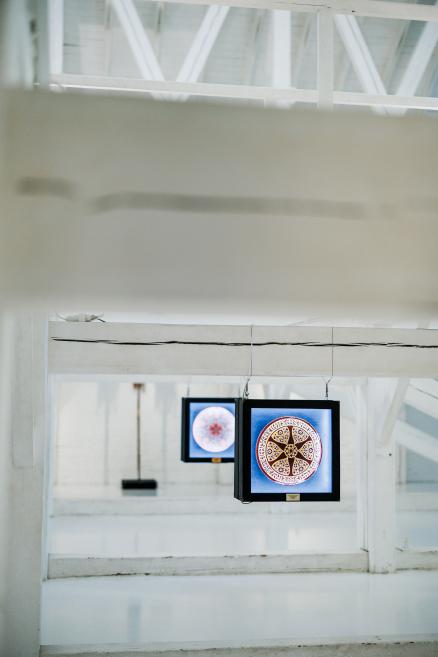 Exhibition view of “Qalqan. Symbols of Crimean Tatars” showing illuminated images of ornamental plates in a white gallery space.