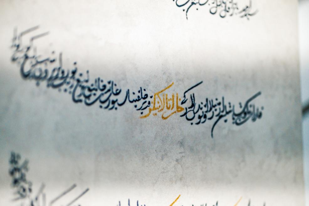 Kaligrāfijas fragments ar melnu un zeltainu arābu rakstu uz gaiša pergamenta no izstādes “Qalqan. Krimas tatāru simboli”.