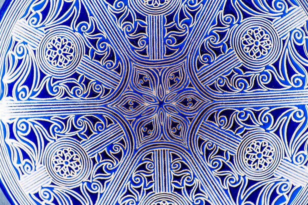 Blue-toned ornamental pattern with fine lines and floral motifs on a plate surface reflecting Crimean Tatar artistic traditions.