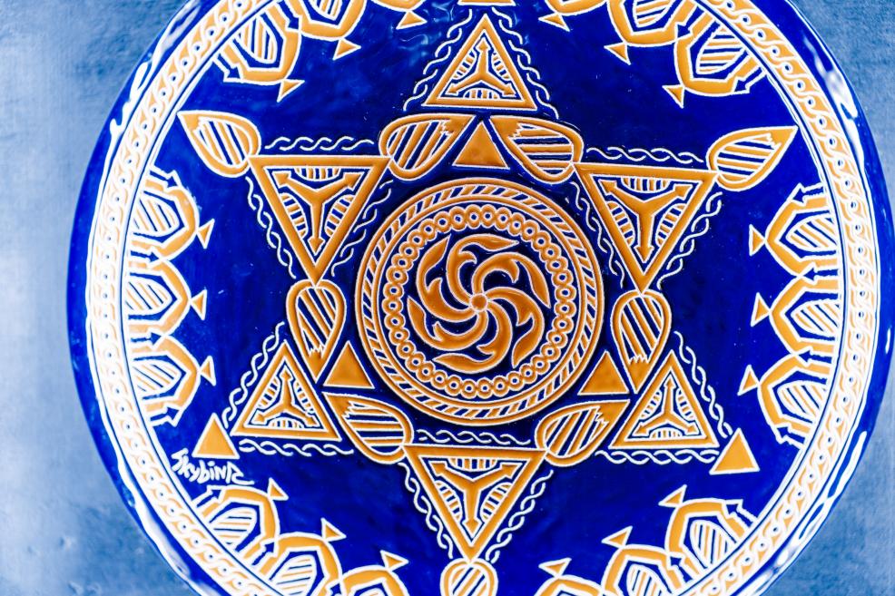 Decorative plate with yellow and blue geometric symbols signed by the artist, a work from the exhibition “Qalqan. Symbols of Crimean Tatars”.