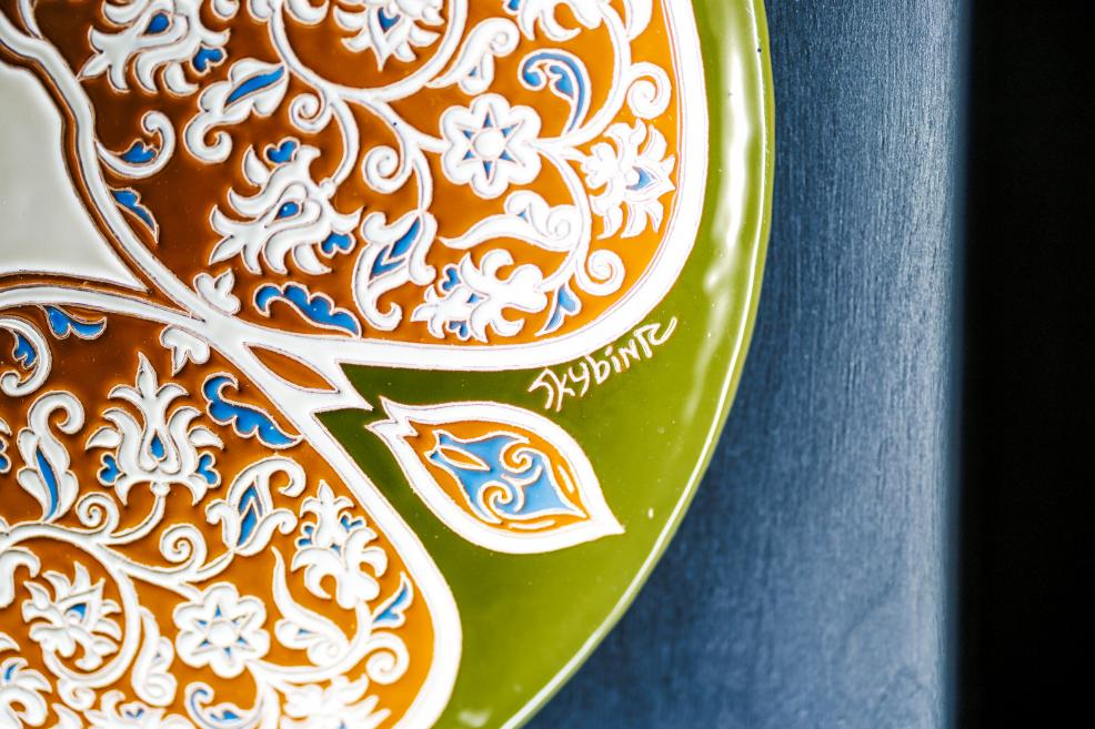 Plate fragment with ornamental floral motifs in orange, green, and blue tones signed by the artist from the exhibition “Qalqan. Symbols of Crimean Tatars”.