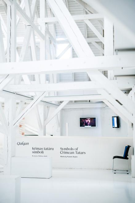 Gallery view of the exhibition “Qalqan. Symbols of Crimean Tatars” with wall text and video screens in the background.