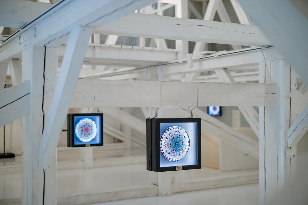 Exhibition view of “Qalqan. Symbols of Crimean Tatars” featuring Rustem Skibin’s illuminated works against white wooden beams.