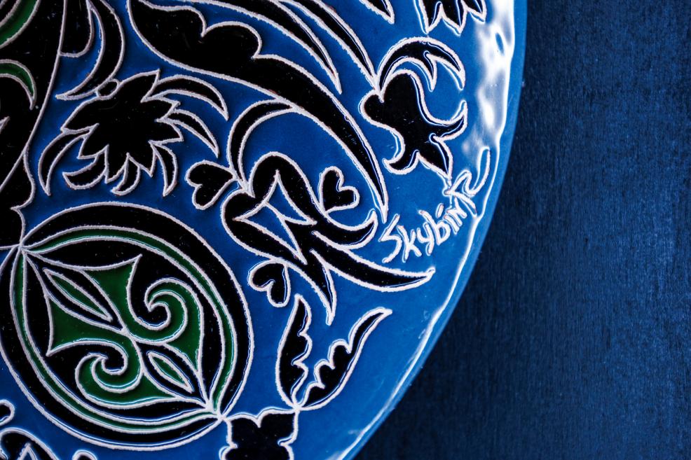 Close-up of Rustem Skibin’s signature on a blue and green ornamental ceramic plate.