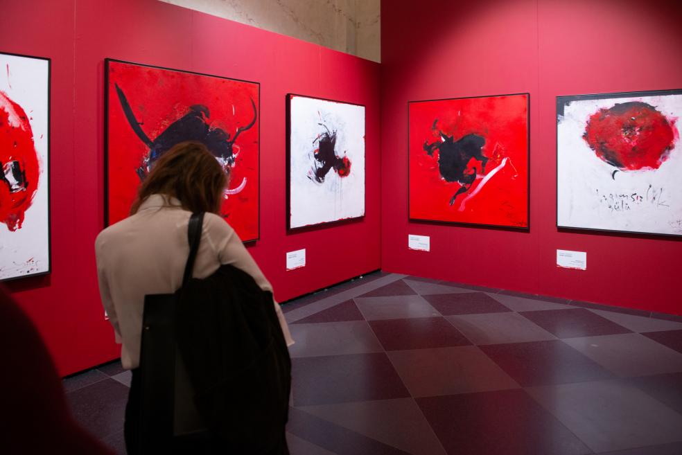 A woman observes expressive red and black artworks in the exhibition hall.