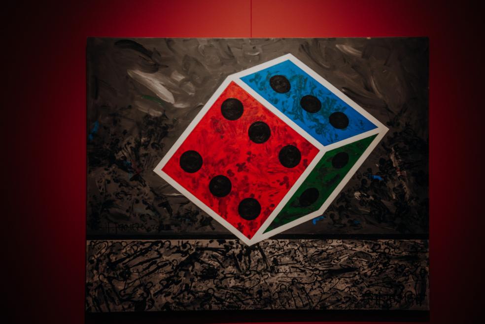 The painting depicts a colorful metamorphic dice on a gray and black background.
