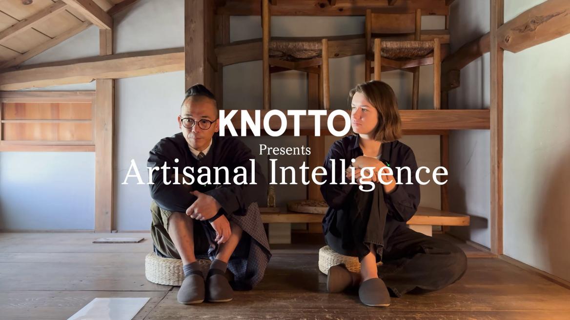 Divi cilvēki sēž uz grīdas tradicionālā koka interjerā, virs attēla redzams uzraksts “KNOTTO Presents Artisanal Intelligence”.