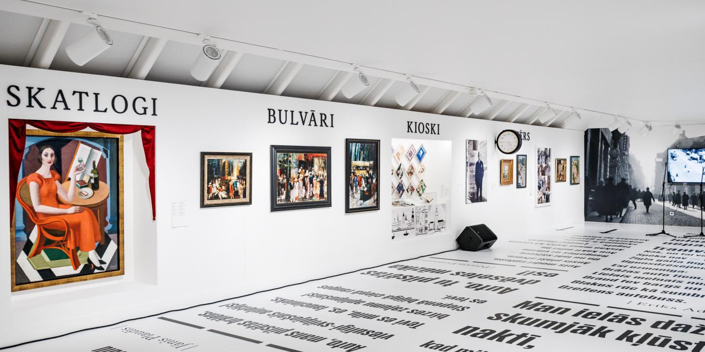 Muzeja ekspozīcijas zāle ar gleznām un fotogrāfijām pie sienas zem uzrakstiem “Skatlogi”, “Bulvāri” un “Kioski”, bet uz grīdas izvietoti liela formāta teksti.