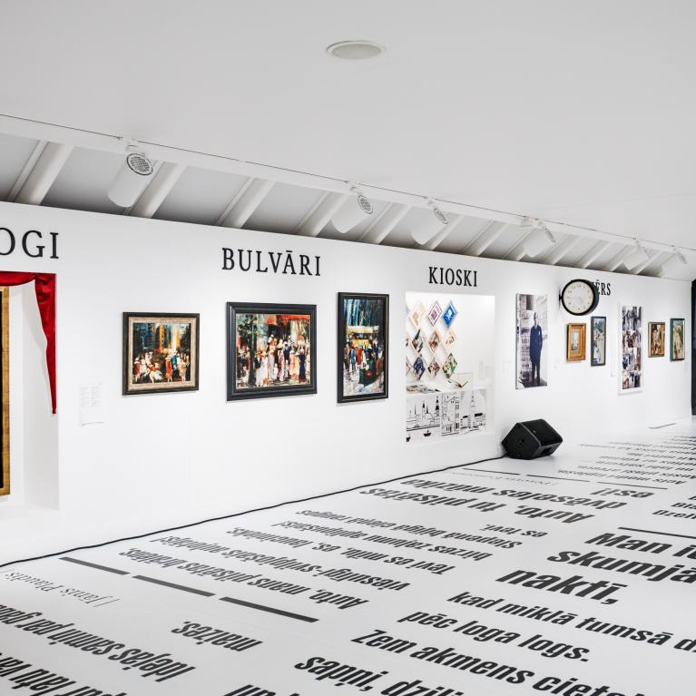 Muzeja ekspozīcijas zāle ar gleznām un fotogrāfijām pie sienas zem uzrakstiem “Skatlogi”, “Bulvāri” un “Kioski”, bet uz grīdas izvietoti liela formāta teksti.