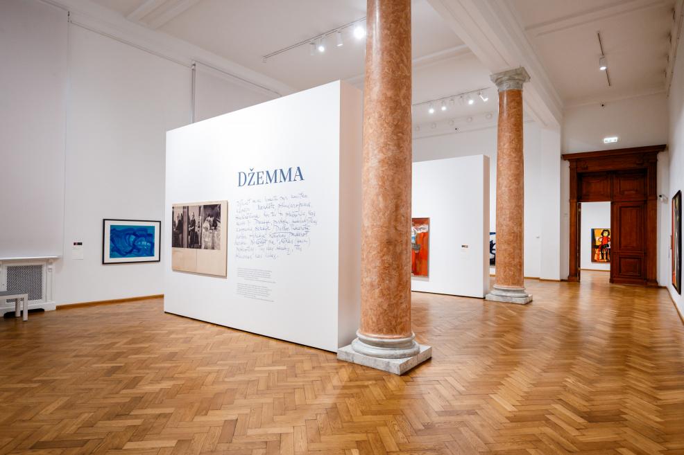 An exhibition hall at the Latvian National Museum of Art shows the display “Džemma” with paintings and wall texts.