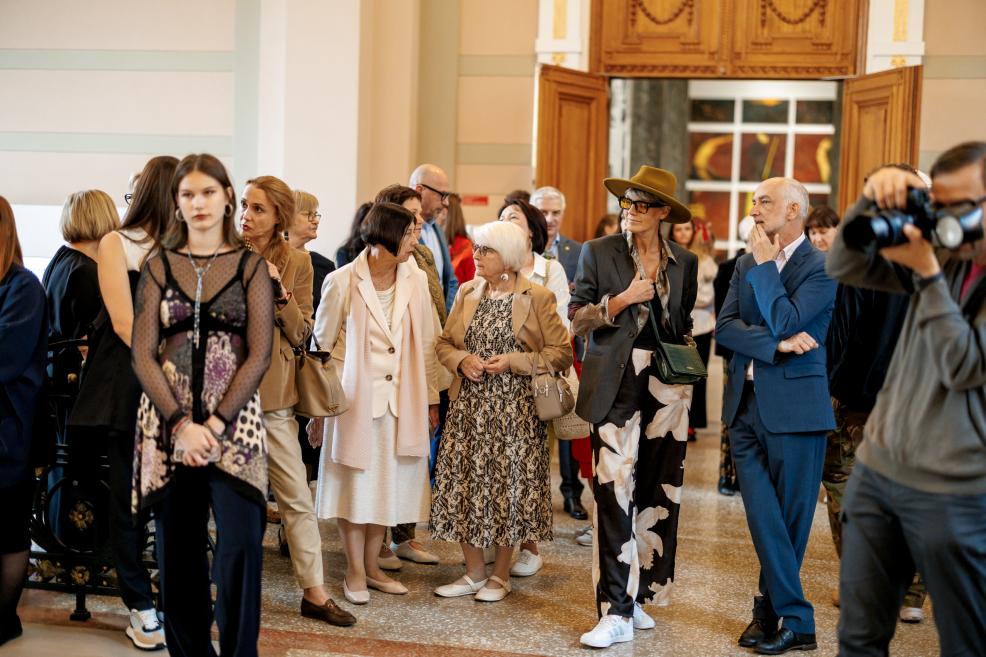 People of different ages gather near wooden doors at the museum exhibition opening.