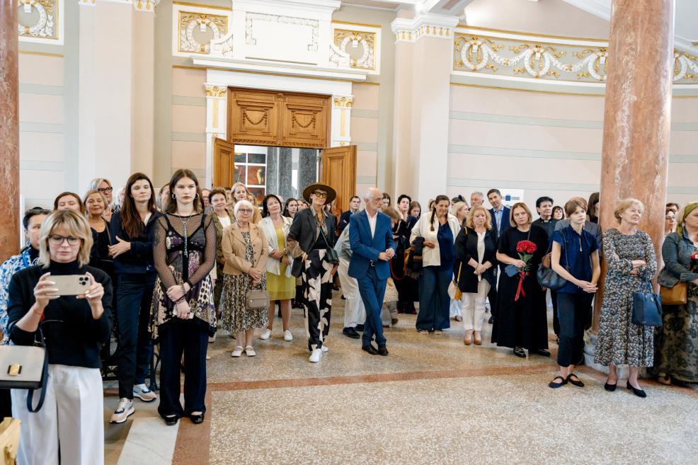 A large group of visitors stands in the museum foyer listening to speeches at the opening of the exhibition “Džemma.”