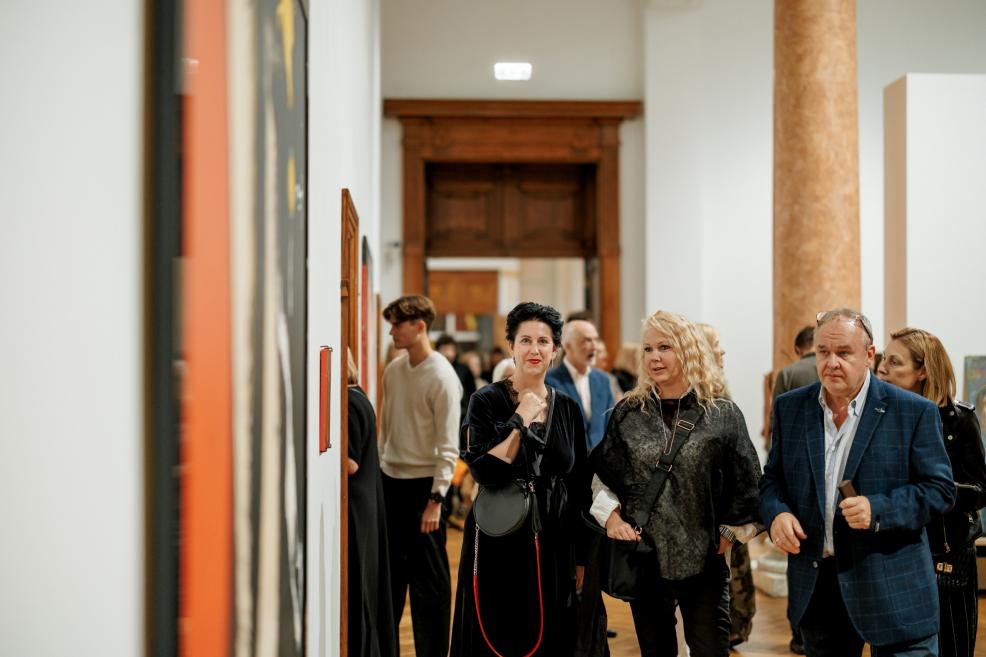 Visitors in the museum hall observe paintings on the wall and engage in conversation.