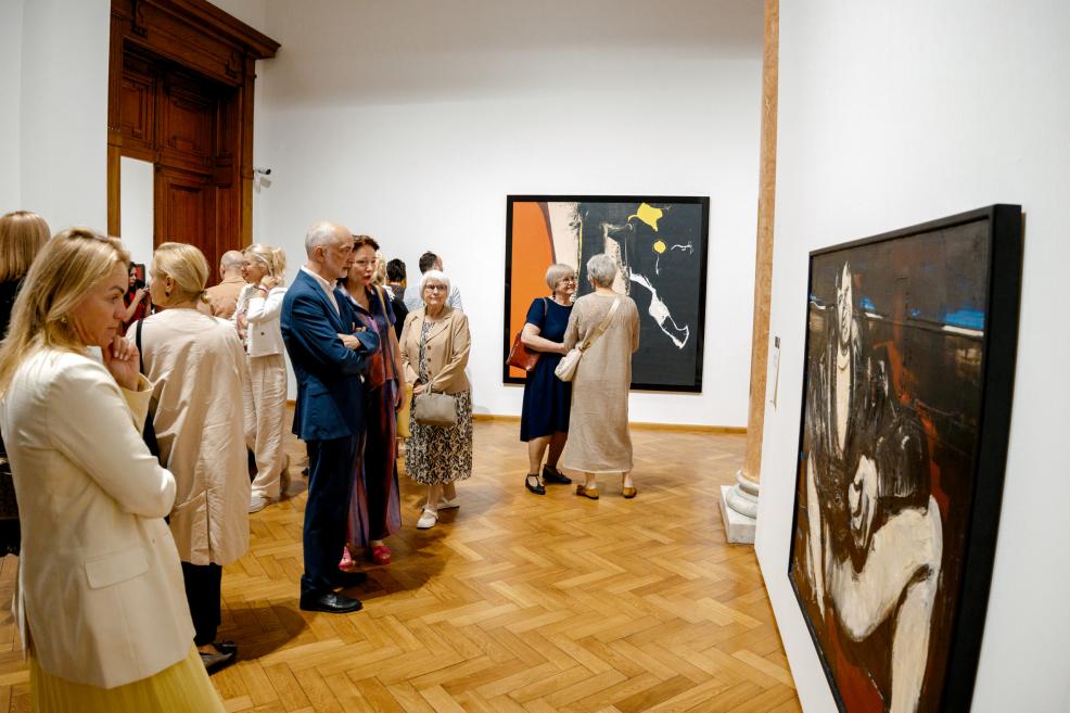 Visitors converse near a large abstract artwork with orange and black color fields.
