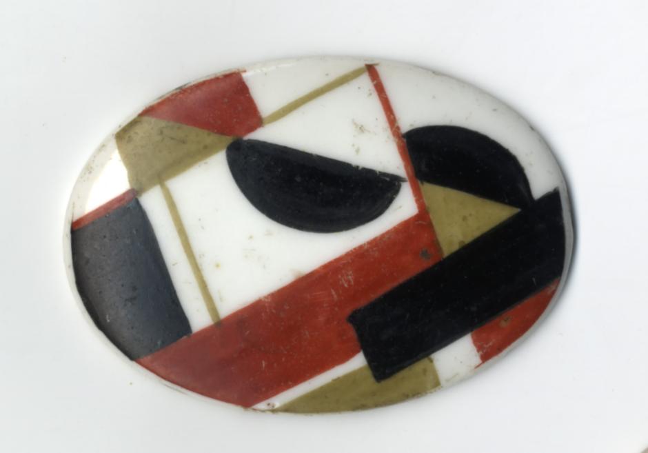 Ovāla dekoratīva porcelāna šķīvīša virsma ar abstraktu ģeometrisku rakstu sarkanā, melnā, baltā un olīvkrāsas toņos.