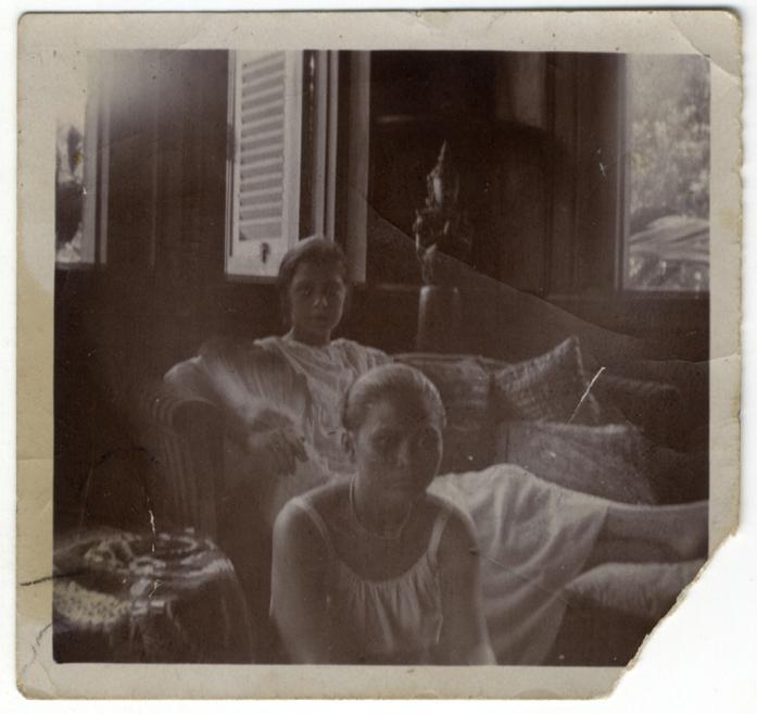 Black-and-white photograph of two women in light dresses seated in a living room by an open window.