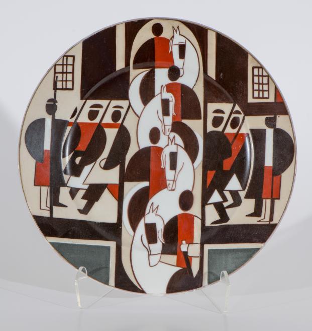 Round decorative plate with a stylized abstract composition in red-brown, white and black tones depicting horses and human figures.