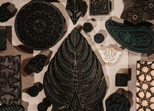 Uz galda izvietoti dažādu formu un rakstu koka spiedogi tekstila apdrukai.