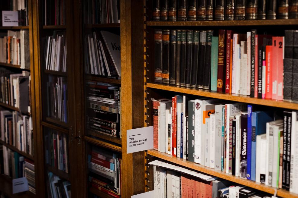 Mākslas literatūras plaukti Latvijas Nacionālā mākslas muzeja bibliotēkā ar redzamiem uzrakstiem par tematiskajām sadaļām.