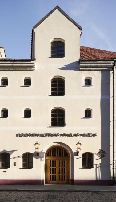 Dekoratīvās mākslas un dizaina muzeja fasāde Vecrīgā ar koka durvīm un vēsturisku uzrakstu virs ieejas.