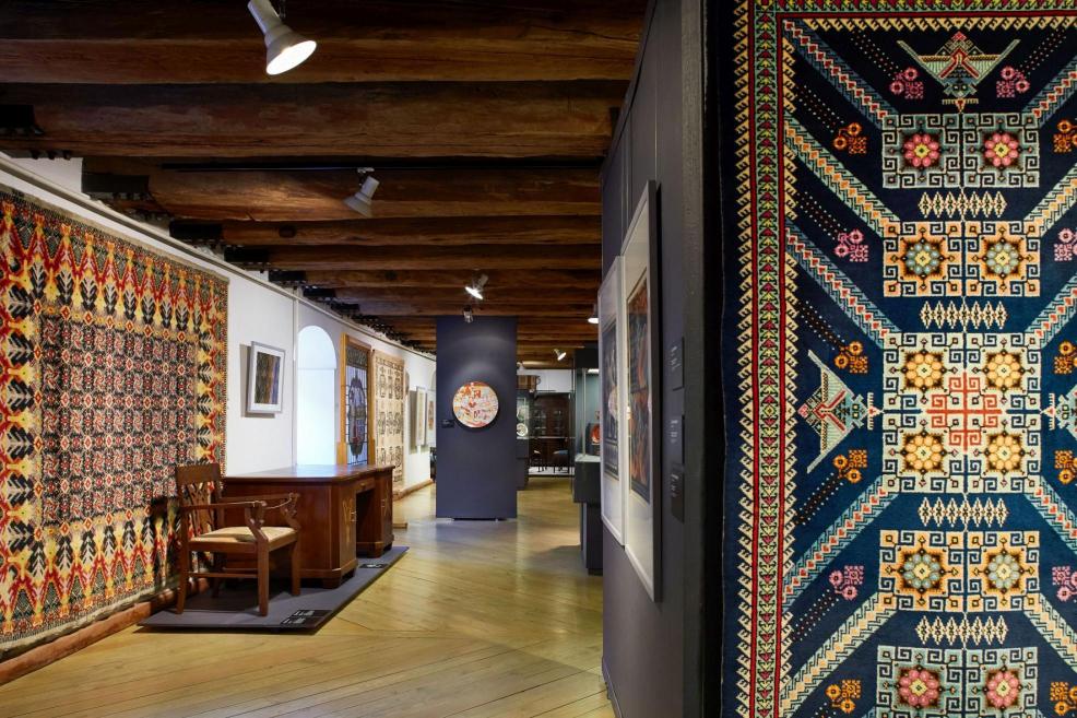 Dekoratīvās mākslas un dizaina muzeja ekspozīcija ar krāsainiem tekstila darbiem un mēbelēm vēsturiskā interjerā.