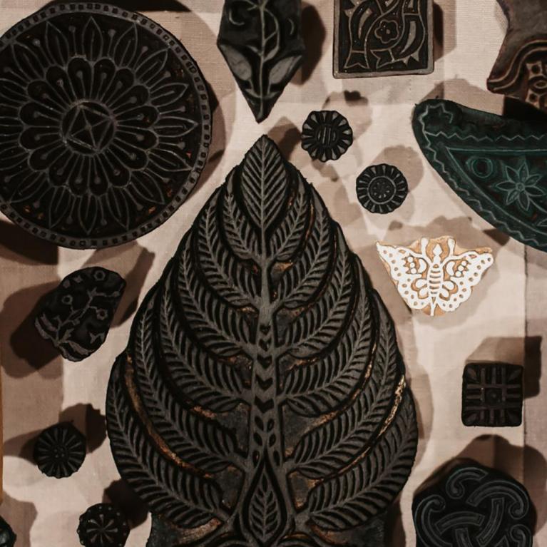 Uz galda izvietoti dažādu formu un rakstu koka spiedogi tekstila apdrukai.