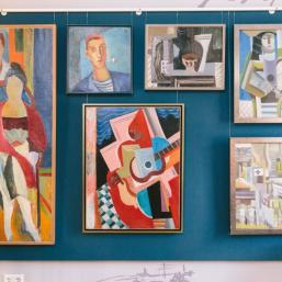 Colorful cubist-style paintings depicting figures and city scenes displayed on a wall.