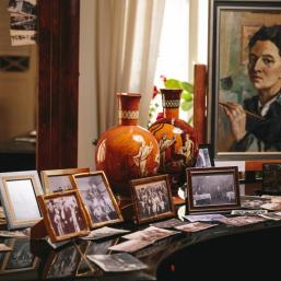 Framed photographs and two decorative vases displayed on a piano, with a portrait visible in the background.