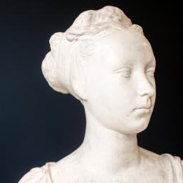Bust of a woman, a white marble sculpture featuring delicately modeled hair and a serene facial expression.