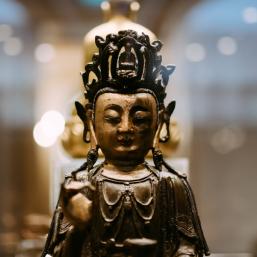 Close-up of a bronze Buddhist deity sculpture in a museum exhibition.