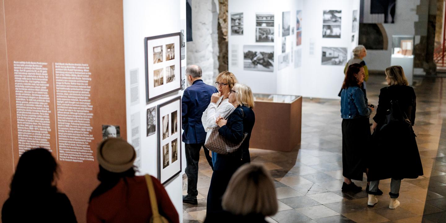 Apmeklētāji iepazīstas ar fotogrāfijām un teksta ekspozīciju plašā izstāžu zālē.