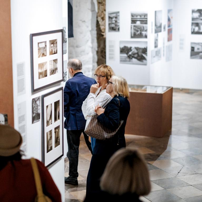 Apmeklētāji iepazīstas ar fotogrāfijām un teksta ekspozīciju plašā izstāžu zālē.