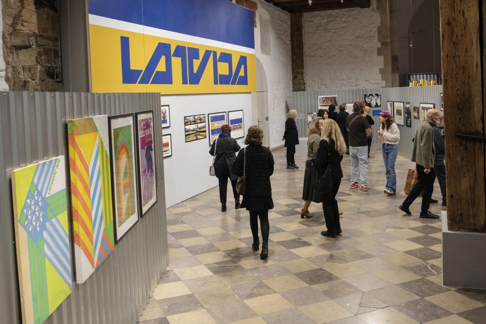 Visitors in the exhibition room near the sign "Latvija"