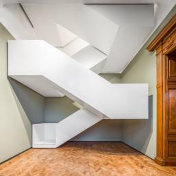A modern white staircase structure in the interior of the Latvian National Museum of Art, contrasting with the historic wooden doorway.