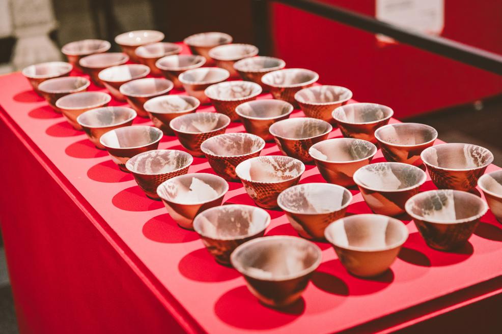 Small ceramic bowls are neatly arranged in rows on a red pedestal.