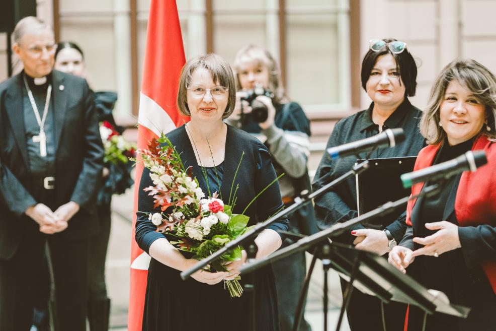 A woman holding a bouquet of flowers receives congratulations during a formal moment.