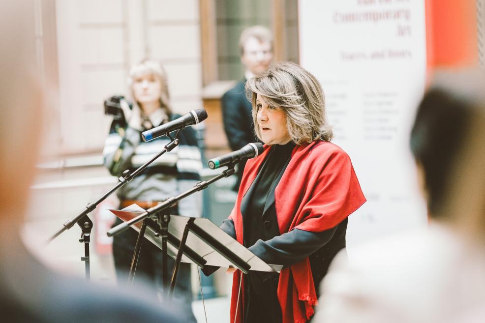 A woman with a red shawl speaks at a formal gathering.