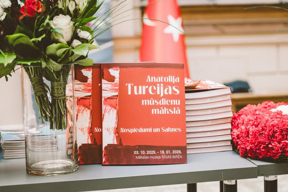 Catalogues with red covers, flowers, and a flag are displayed on a table.