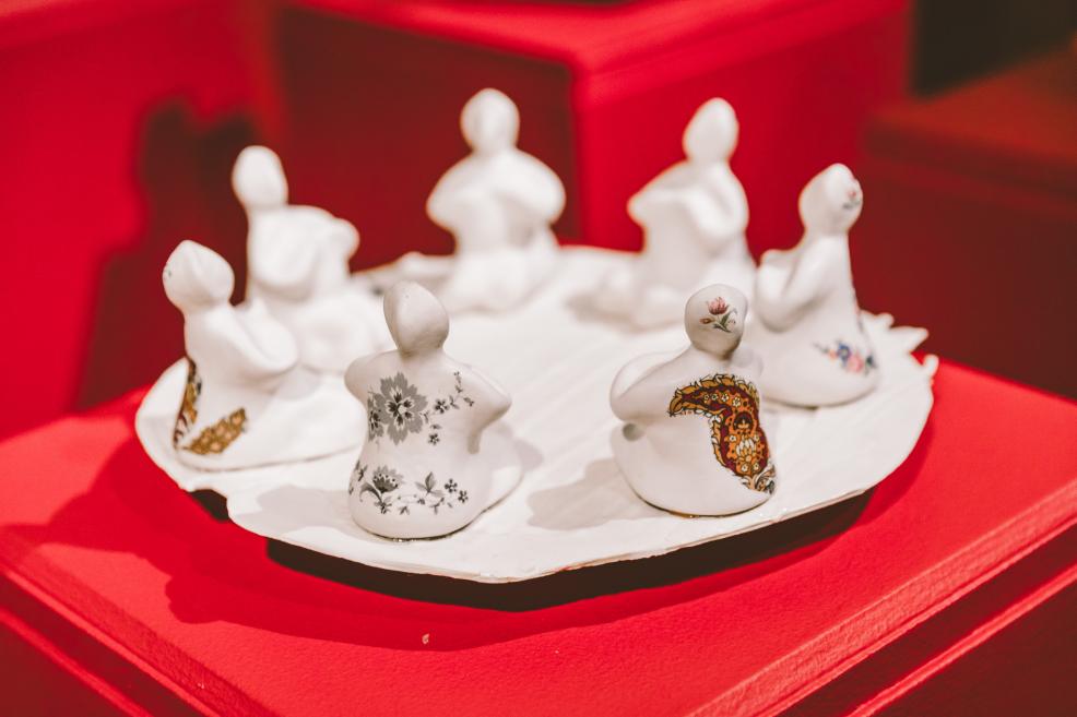 White ceramic figures with ornaments are arranged on a plate atop a red pedestal.