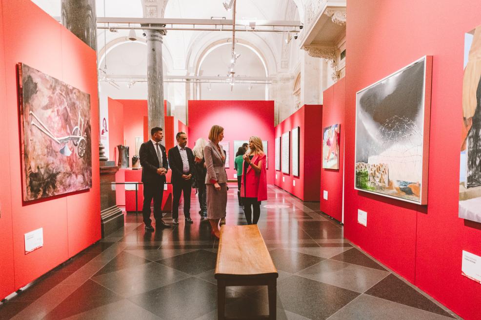 Guests observe paintings and ceramic works in a gallery with red walls.